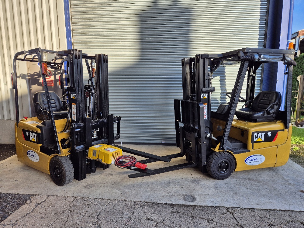Two yellow CAT forklifts outside a workshop